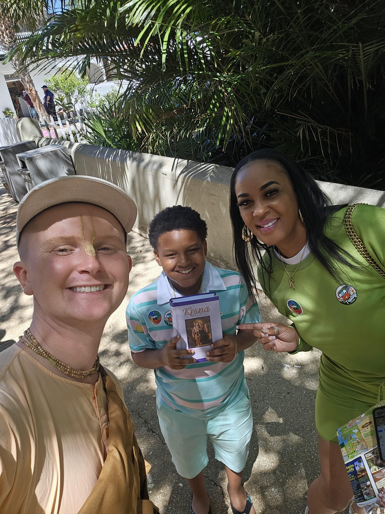 A devotee and two smiling people holding a Krishna book